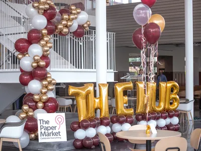 Bright, well-lit party supply store with colorful balloon displays, gift packaging options, and a central table of white...