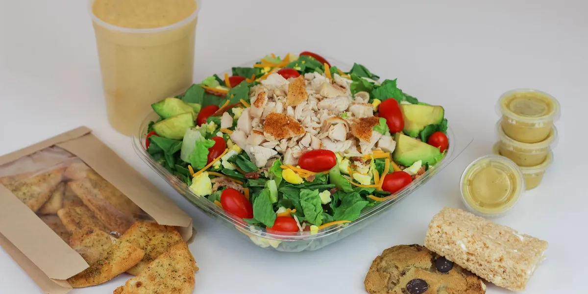 Bright, clean salad bar station with fresh ingredients displayed in neat rows, families selecting toppings at the counter.