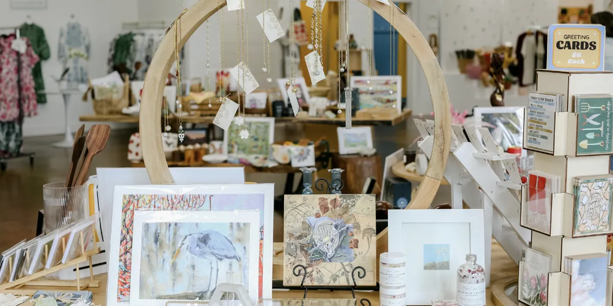 Bright boutique interior with diverse vendor booths displaying locally-crafted art, home decor, and unique gifts arranged...
