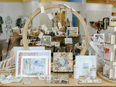 Bright boutique interior with diverse vendor booths displaying locally-crafted art, home decor, and unique gifts arranged...
