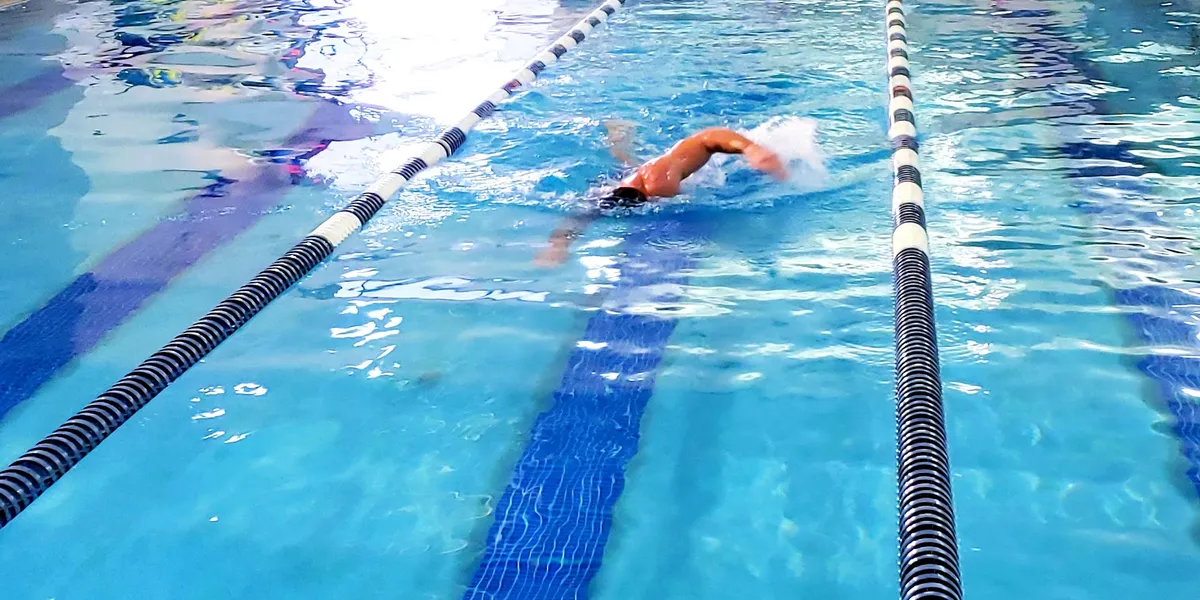 Bright, chlorine-scented fitness facility with an indoor pool, hot tub area, and exercise equipment spread throughout the...