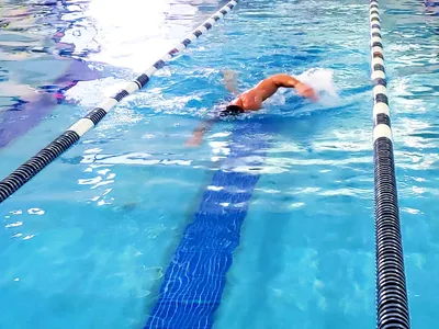 Bright, chlorine-scented fitness facility with an indoor pool, hot tub area, and exercise equipment spread throughout the...