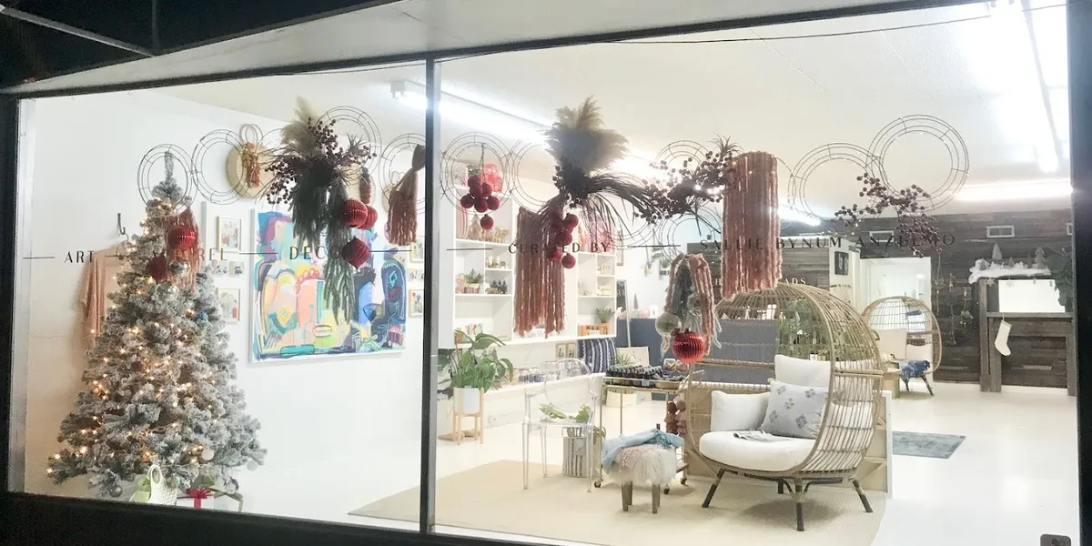 Bright boutique with displays of handcrafted glassware, original paintings, and eclectic jewelry arranged throughout a...