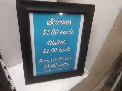 Bright, organized thrift store with neatly arranged sections, handcrafted faith items displayed prominently, and women...