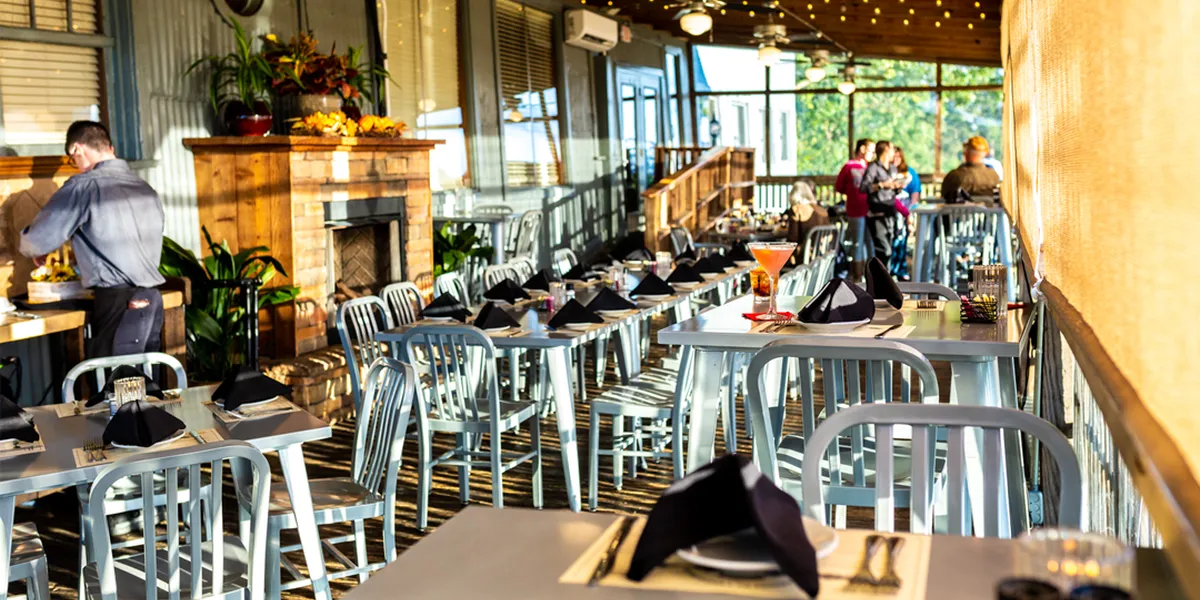 Historic warehouse restaurant with riverside patio seating, elegant dining room with piano player, and sunset views over...