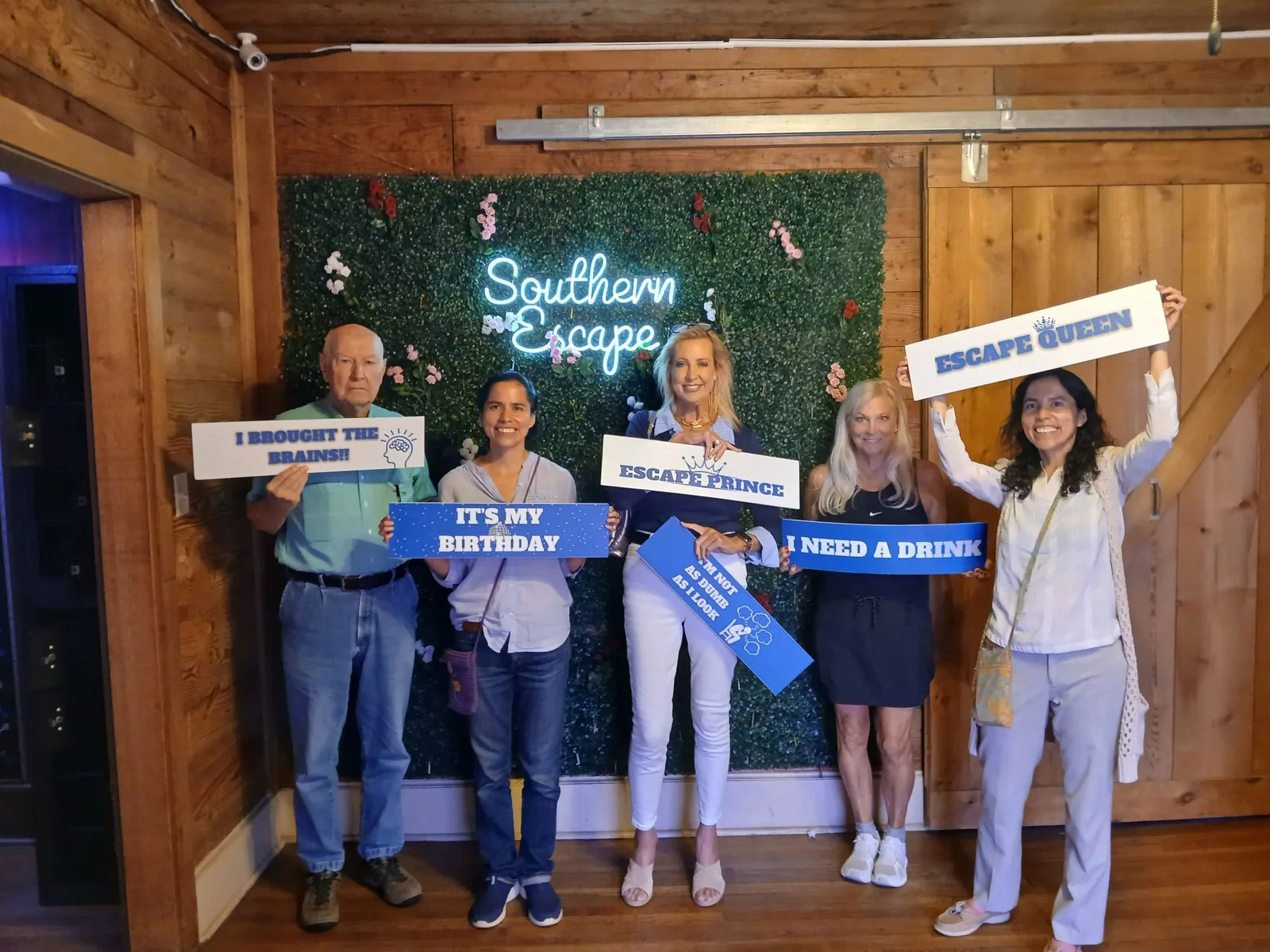 Group with escape room props posing at the Southern Escape neon sign in Monroe Louisiana