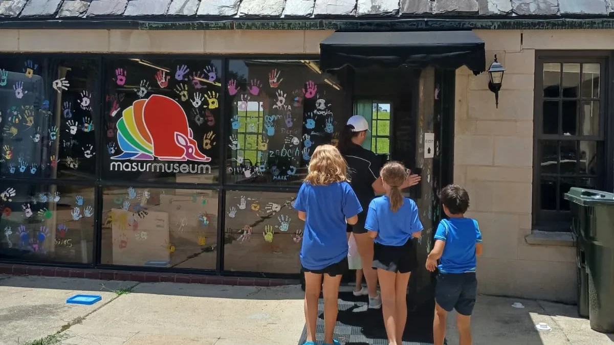 Masur Museum carriage house entrance in Monroe, Louisiana, with the museum logo and colorful handprints covering the windows, children arriving for the MasurKIDS drop-in