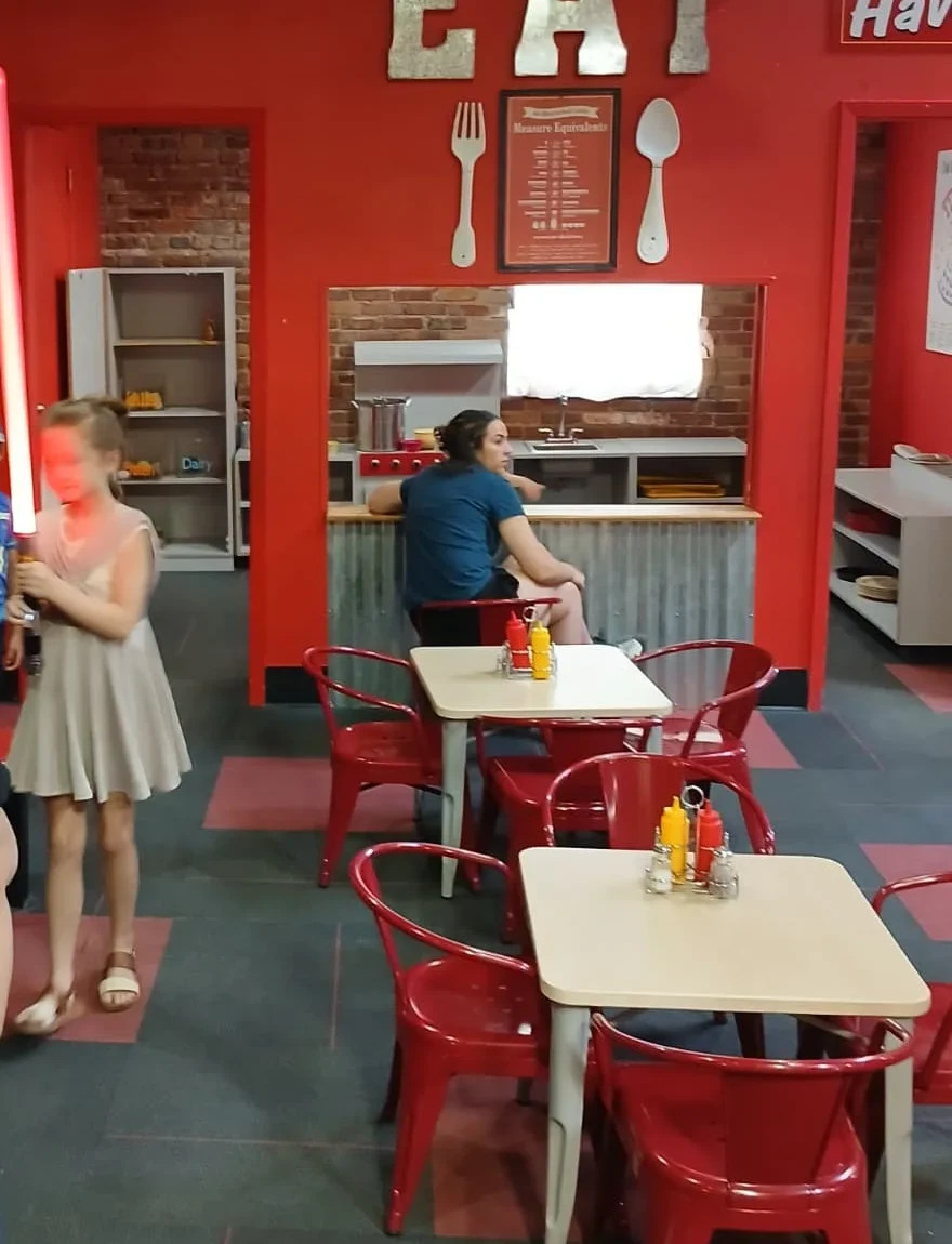 Girl holding a glowing red lightsaber inside the Kids Cafe exhibit at the Northeast Louisiana Children's Museum during the 501st Legion Star Wars event